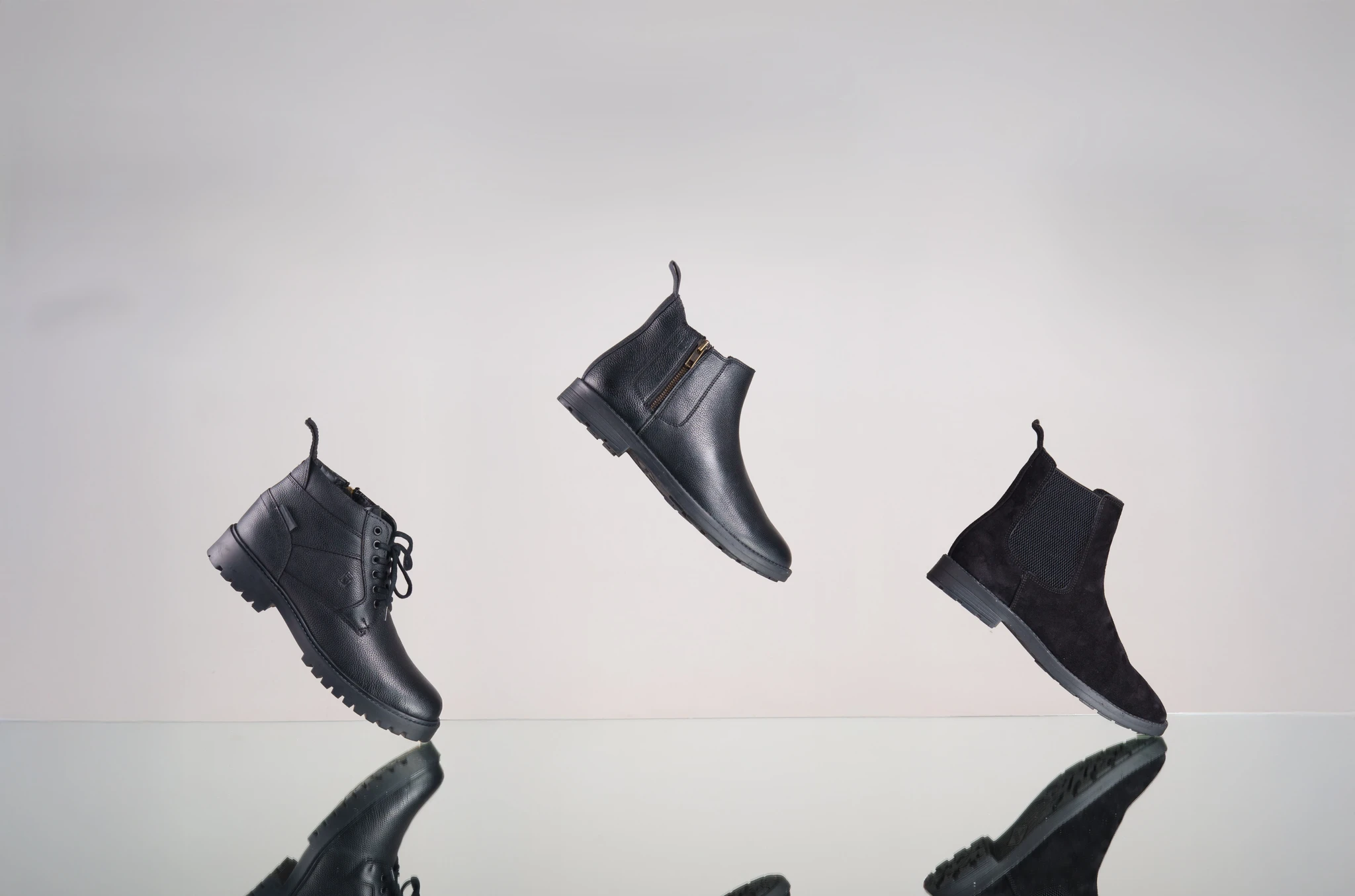 Three handcrafted leather boots suspended above a reflective surface